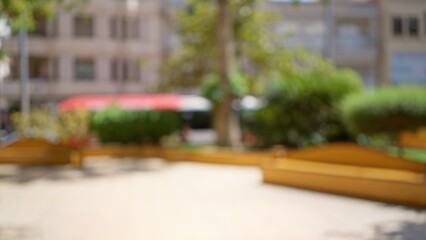 Outdoor blurred background in a sunny park with trees and benches under bright daylight creating a bokeh effect
