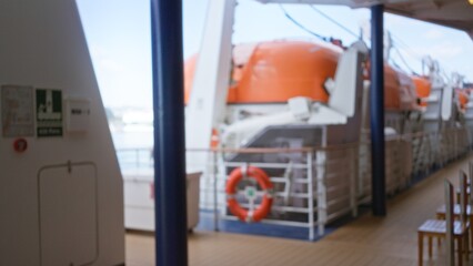 Blurred view of a cruise ship deck featuring lifeboats and safety equipment, highlighting the nautical theme and vibrant outdoor setting on a sunny day.