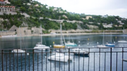 Blurred view of a scenic port with defocused boats afloat, set against a lush green backdrop, creating a serene beachside bokeh effect that captures coastal tranquility.