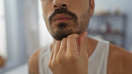 Young hispanic man with beard in indoor spa setting gently touching his chin