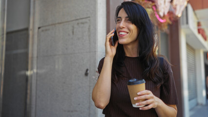 Young woman talking on phone holding coffee cup while standing on city street