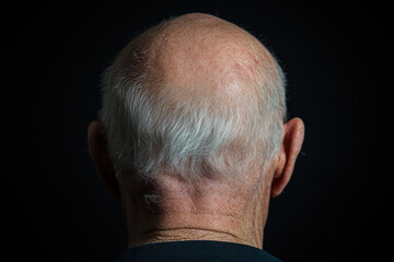 Senior man showing bald head and gray hair on black background