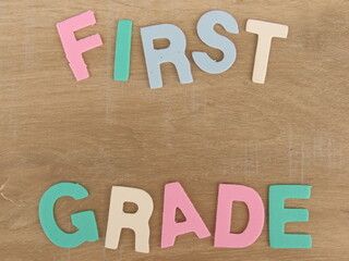 Multicolored eva foam letters form the expression "First grade", referring to the elementary school days. Light wood background. Back to school concept.