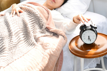 ベッドで起床後に目覚まし時計を止める女性