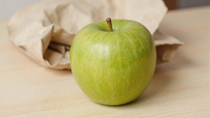 Fresh green apple on table beside crumpled paper bag Classic kitchen setting