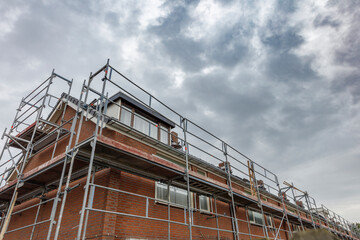 Scaffolding surrounds a row of brick houses under a cloudy sky.  Construction is underway.