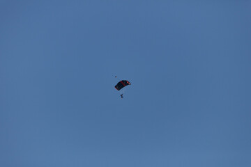Parachutist with open parachute floats in a clear blue sky.  Perfect sunny day.