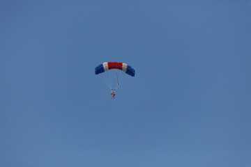 Two people in a red, white, and blue parachute glide through a clear blue sky.