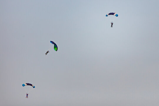 Several skydivers with colorful parachutes descend.  A gray, overcast sky is the backdrop.