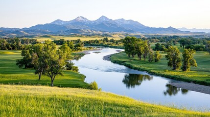 Fototapeta premium Serene river meandering through lush green valley, majestic mountains in background.