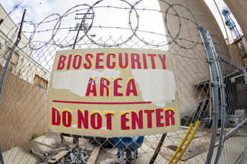 Obraz premium A fishe eye effect of a sign stating Biosecurity Area Do Not Enter surrounded by barbed wire and a fence. The sign has red letters and is in disrepair
