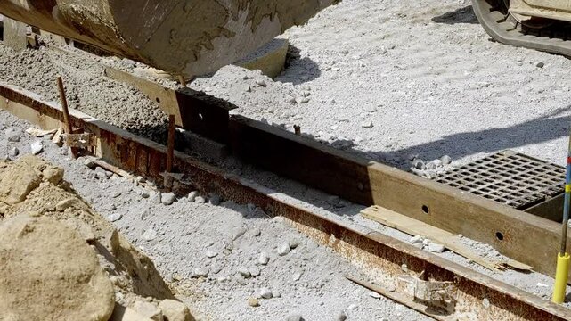 Construction worker pouring and leveling fresh concrete at a job site in bright sunlight