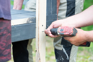 Screwing the board with a screwdriver, installing a wooden gazebo.