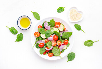 Spring healthy vegetable salad with spinach, tomatoes, cucumber, red onion and olive oil. White background, top view