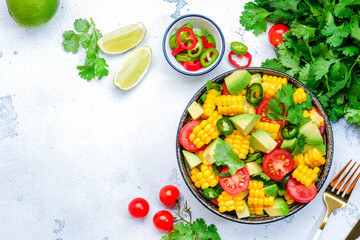 Vegan spicy salad with corn, avocado, jalapeno pepper, tomatoes, cilantro, lime and olive oil. White background, top view