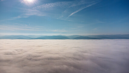 Aerial view of a breathtaking landscape featuring a vast sea of clouds illuminated by the sun, with majestic mountain peaks rising in the distance