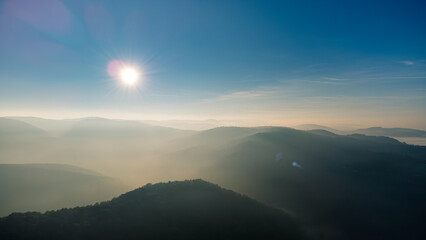 Fototapeta premium Capturing an aerial view of endless mountain ridges disappearing into the fog, illuminated by the bright morning sun at sunrise