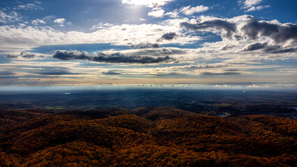 Stunning aerial view of rolling hills covered in vibrant fall foliage under a dramatic cloudy sky, creating a picturesque autumn scene