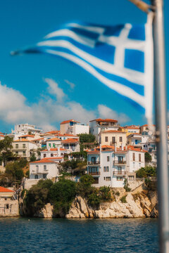 Picturesque coastal village on skiathos island with traditional whitewashed houses under the greek flag waving in the wind