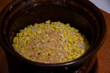 A clay pot filled with freshly cooked rice mixed with sweet corn kernels, creating a simple and warm Japanese dish with a natural sweetness.