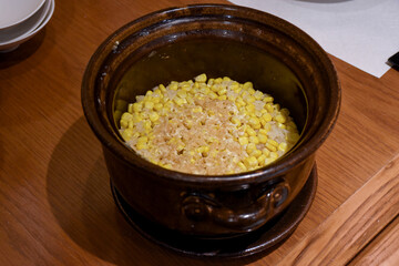 A clay pot filled with freshly cooked rice mixed with sweet corn kernels, creating a simple and warm Japanese dish with a natural sweetness.