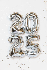 New year 2025 balloon celebration card. Silver foil helium balloons number 2025, party decoration, silver confetti stars on white background. Flat lay, merry christmas, happy holidays concept.