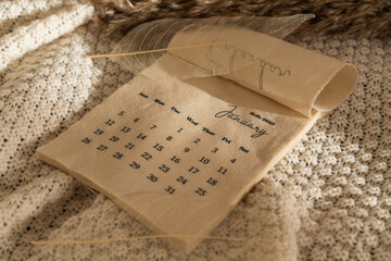 Beige linen fabric calendar 2025 with January month 2025 and dry branch on a knitted blanket with copy space. Flat lay, New Year template. Minimal top view aesthetic composition	