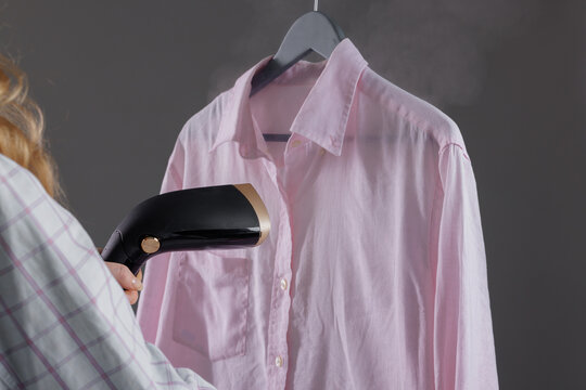 Woman steaming clothes on hanger at home, close up, handheld steamer in woman's hand