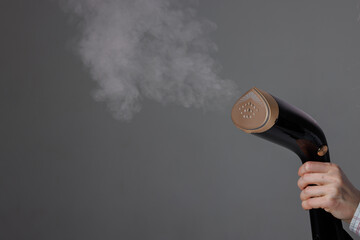 handheld steamer in woman's hand with steam on grey background, close up © st.kolesnikov