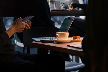 A person holding a smartphone in a dimly lit café, with a coffee cup, tablet, and keyboard on the...