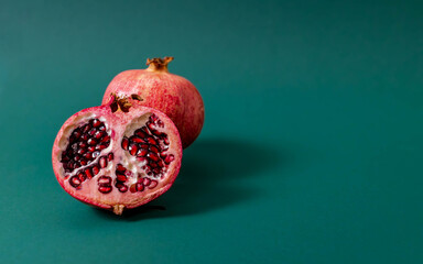 A halved pomegranate displaying vibrant red seeds placed in front of a whole pomegranate on a green...