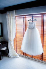 Elegant Wedding Gown Hanging in Sunlit Bedroom Interior