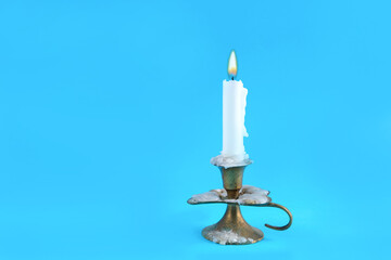 Very old retro candle in a candlestick with a burning flame on a classic blue background in a studio. Fire and minimalism concept with copy space for text or design