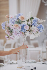Wedding decoration with flowers. Professional florist decorator using beautiful flowers making composition wedding table. A woman puts a vase with flowers on table. 