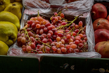 Crates filled with fresh red grapes, pomegranates, and quince at a market stall, showcasing a vibrant and natural display of seasonal fruits.