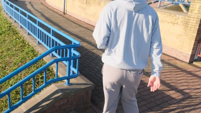 Man in light blue hoodie climbs outdoor steps with blue railings. Active workout, fitness training