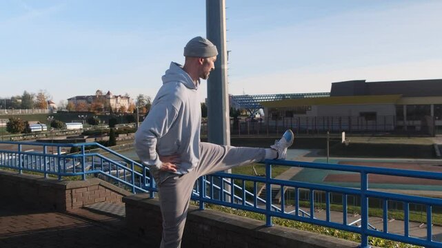 Athlete warming up, stretching leg on blue railing outdoors. Fitness and healthy lifestyle concept