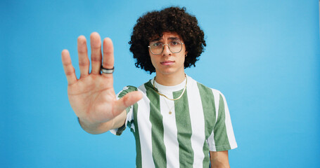 Man, portrait and hand with stop for rejection, no or protest on a blue studio background. Male...