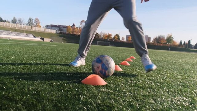Football training, close-up on feet. Athlete dribbles a soccer ball between orange cones. Sunny day on field