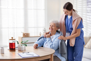 Caregiver covering senior woman with blanket indoors. Home health care service