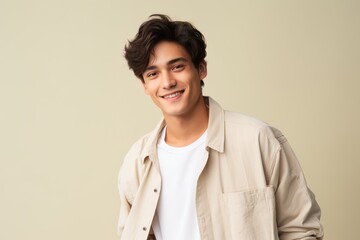 A young man is smiling and wearing a white shirt and tan jacket