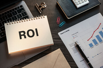 There is notebook with the word ROI. It is an abbreviation for Return On Investment as eye-catching...