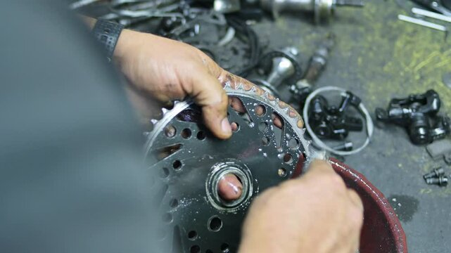 Hands view of mechanic man cleaning bicycle chainring on work desk in bikeshop