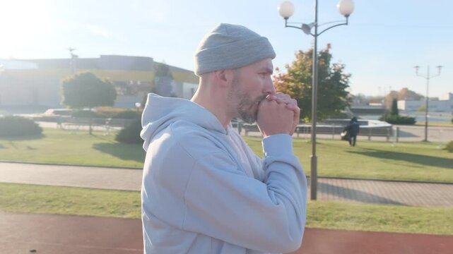 Athlete preparing for training, rubbing his hands together. He wears a grey beanie and light blue hoodie