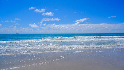 A Serene Beach View With A Stretch Of Turquoise Water With A Sky Decorated With Fluffy White Clouds On A Clear Blue Canvas.