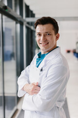 Young handsome doctor looking at the camera, holding a patient’s chart and pen in a modern clinic