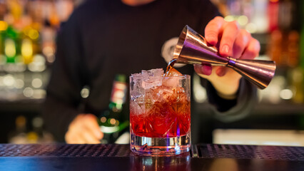 The bartender pours a red cocktail. 