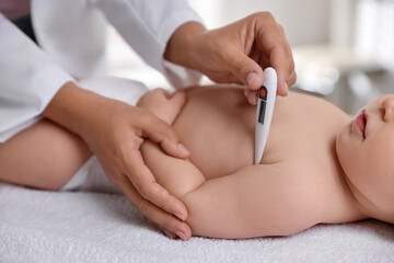 Pediatrician examining little child with thermometer in clinic, closeup. Checking baby's health
