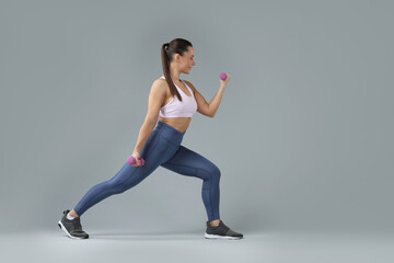 Fototapeta premium Woman exercising with dumbbells on light grey background, space for text