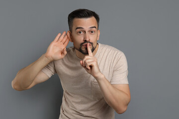 Man showing hand to ear gesture on grey background